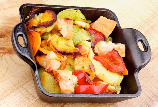Delicious Homemade Salmon Stew with Potato, Red Bell Pepper, Leek and Carrot in Black Frying Pan closeup on Wooden background