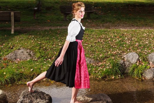 Beautiful barefoot woman playing in a mountain stream in a traditional German dirndl as she enjoys nature