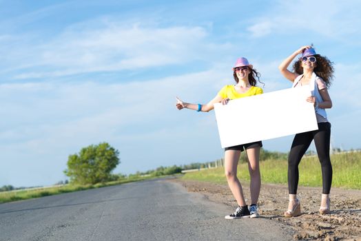 Two young women stand with a blank banner on the side of the road, place for text