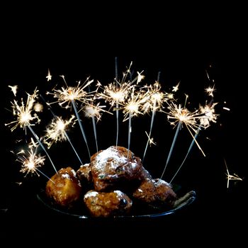 a pile with oliebollen with fireworks on a plate on a white background