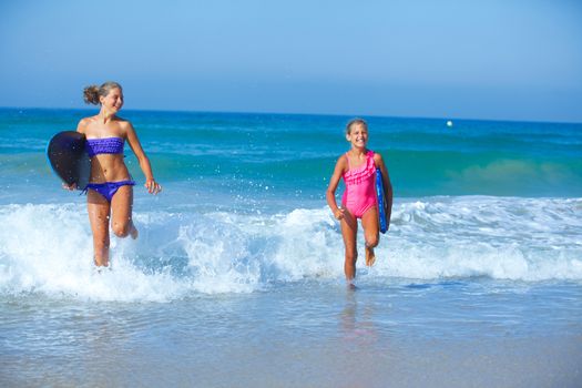 Summer vacation - Two cute girls in bikini with surfboard running from the ocean.
