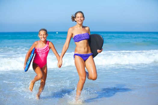 Two cute girls in bikini with surfboard running from the ocean