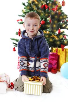 Smiling boy holding present under Christmas tree over white