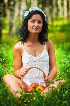 Beautiful girl sitting on grass floor and holding basket of apples