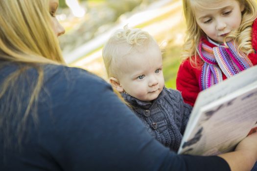 Mother Reading a Book to Her Two Adorable Blonde Children Wearing Winter Coats Outdoors.
