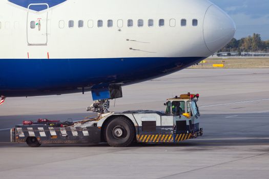 Large aircraft being pulled by airport tug tractor taxing on airfield into docking position for passenger boarding the airplane