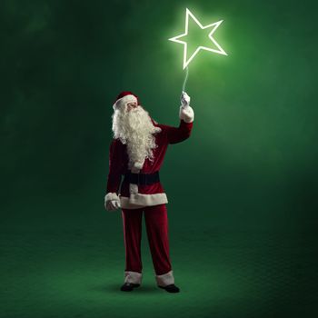 Santa Claus is holding a shining star sign on a string