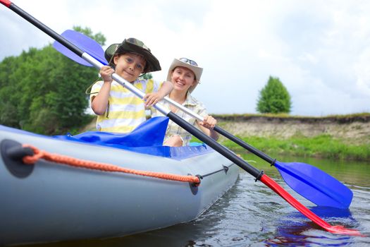 Happy little boy with mother paddling kayak on the river in lovely summer day