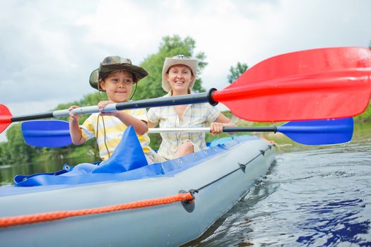 Happy little boy with mother paddling kayak on the river in lovely summer day