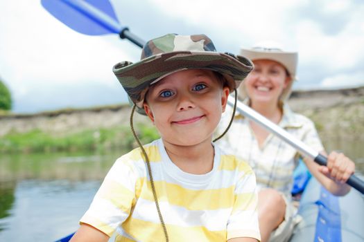 Happy little boy with mother paddling kayak on the river in lovely summer day