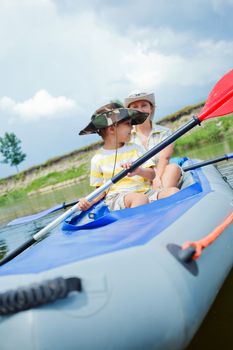 Happy little boy with mother paddling kayak on the river in lovely summer day