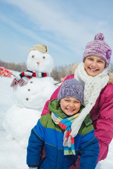 Happy beautiful children with snowman outside in winter time