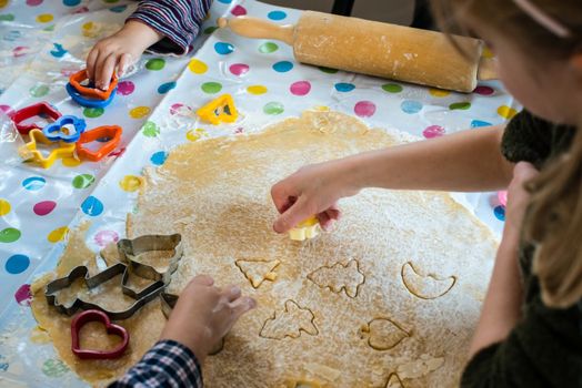 Children baking Christmas cookies: Cutting pastry with a cookie cutter on a colorful table cloth