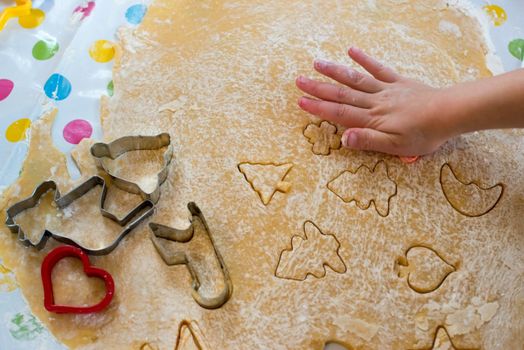 Children baking Christmas cookies: Cutting pastry with a cookie cutter on a colorful table cloth