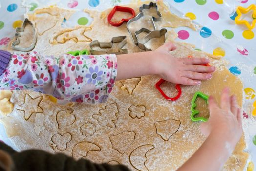 Children baking Christmas cookies: Cutting pastry with a cookie cutter on a colorful table cloth