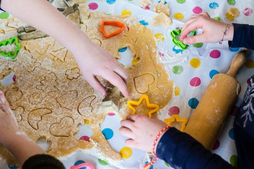 Children baking Christmas cookies: Cutting pastry with a cookie cutter on a colorful table cloth