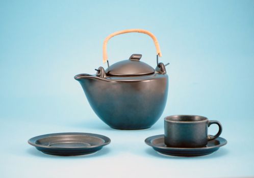 composition retro black teapot tea pot and small cup empty saucer for morning hot drink on blue background.