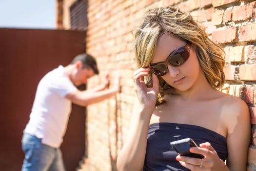 Angry woman in focus looking phone and frustrated man posing his hands on the wall background