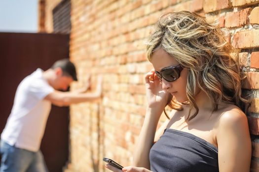 Angry woman in focus looking phone and frustrated man posing his hands on the wall background
