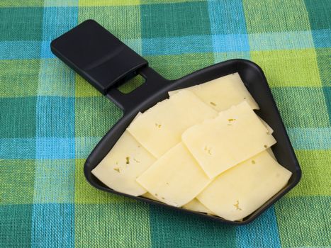 Raclette pan with edam cheese on colorful tablecloth