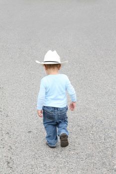 Toddler cowboy walking down the street captured back