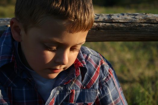 Blond boy sitting outside against a wooden fence
