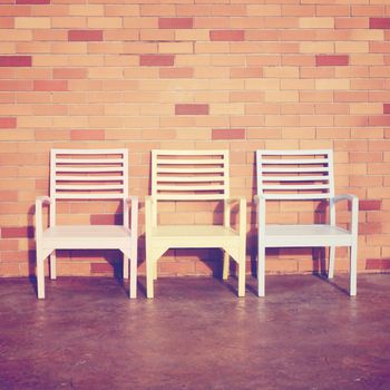 Three wooden chairs with brick wall, retro filter effect