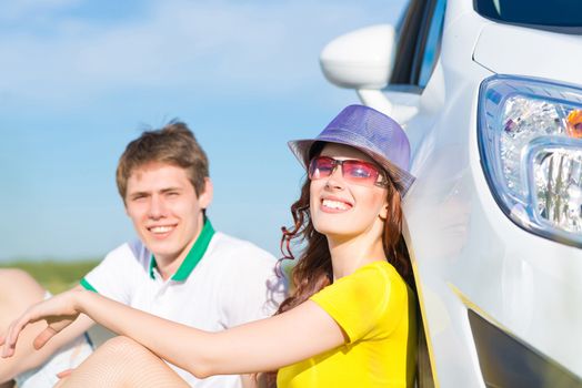 young couple sitting on the ground next to the wheel of a car, a summer road trip