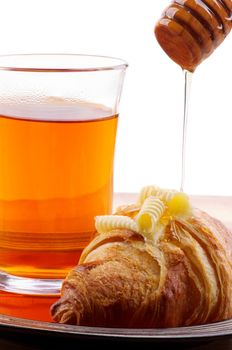 Freshly Baked Croissant with Butter, Honey Dripped from Wooden Dipper  and Cup of Tea closeup