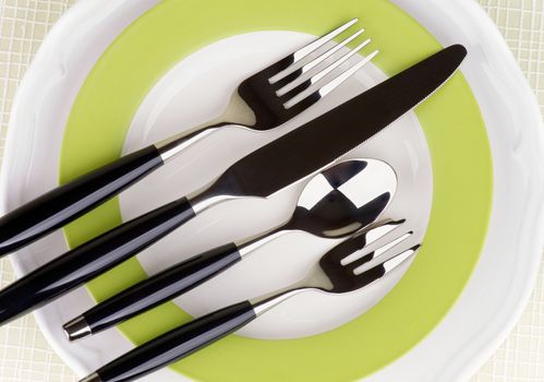Elegant Table Setting with Fork, Table Knife, Spoon and Dessert Fork with Black Handles on White and Green Plates. Top View