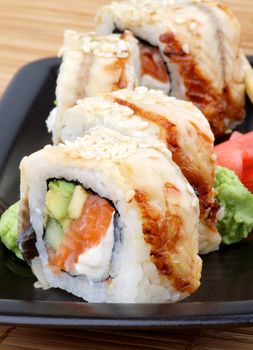 Arrangement of Unagi Sushi Rolls with Wasabi and Marinated Ginger on Black Plate closeup on Straw mat background