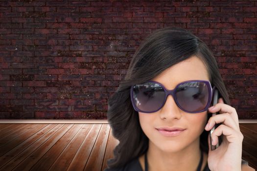 Composite image of elegant brunette wearing sunglasses on the phone in room with brick lined wall