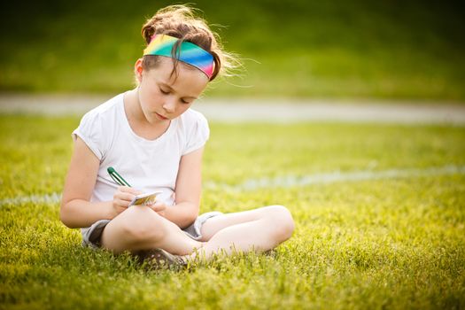 Little girl writing outside on the grass at the golden hour