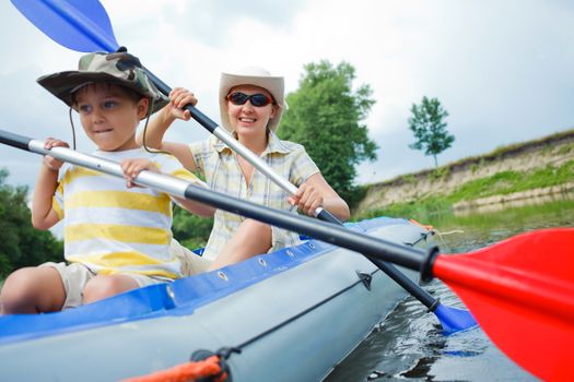 Happy little boy with mother paddling kayak on the river in lovely summer day