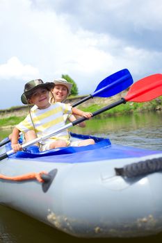 Happy little boy with mother paddling kayak on the river in lovely summer day