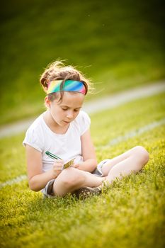 Little girl writing outside on the grass at the golden hour