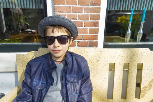 Boy with glasses sitting on a bench in front of the house, The Netherlands