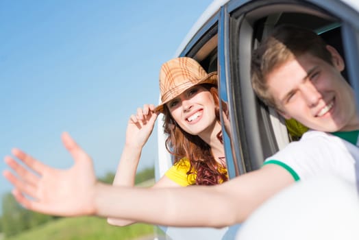 Young woman looking out of car window, holds the hand hat and smiling