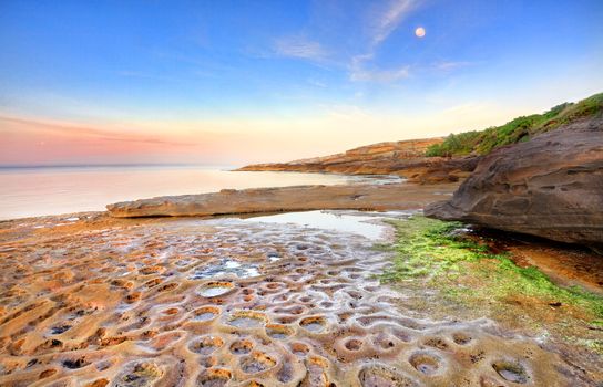 Sunrise at Botany Bay, La Perouse, Sydney Australia on a calm summers morning, the moon still shining overhead  of the strange moonscape crater like potholes in the rocks below.