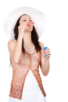 Brunette woman in white sun hat in a white dress, on white background, blowing and makes soap bubble