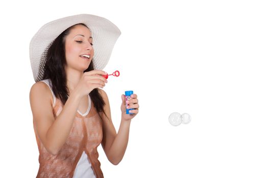 Brunette woman in white sun hat in a white dress, on white background, looking at a flying soap bubble