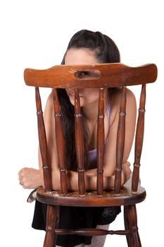 Long-haired brunette woman relies on a chair, is hidden; looking with one eye, isolated on a white background