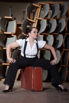 Woman dressed as a man sits on stage at the old suitcase