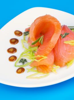 Delicious Snack with Smoked Salmon, Chopped Leek and Mustard Sauce on White Plate closeup on Blue background