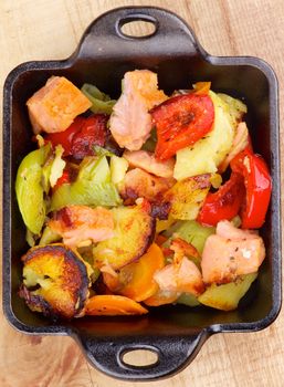 Tasty Homemade Salmon Stew with Potato, Red Bell Pepper, Leek and Carrot in Black Frying Pan on Wooden background. Top View