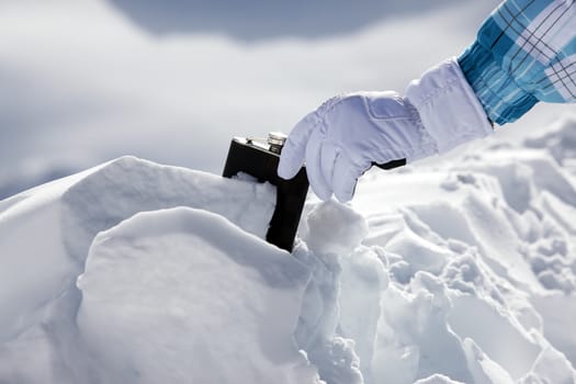 Hipflask in snow and a female hand in a ski glove