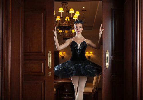 Ballerina in black tutu standing in doorway in luxury interior