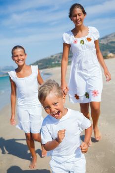 Adorable happy boy with his sisters running on beach vacation