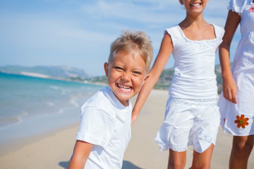 Adorable happy boy with his sisters running on beach vacation