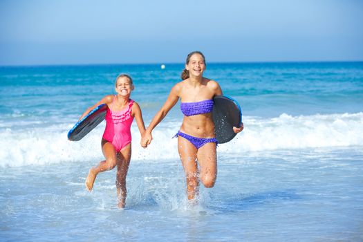 Summer vacation - Two cute girls in bikini with surfboard running from the ocean.